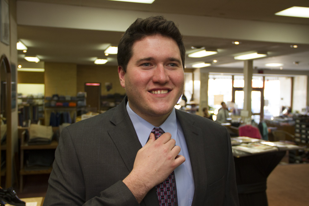 Customer smiling while wearing suit and adjusting tie inside clothing store