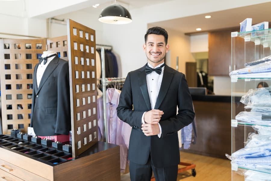 Person smiling while wearing tuxedo in rental store