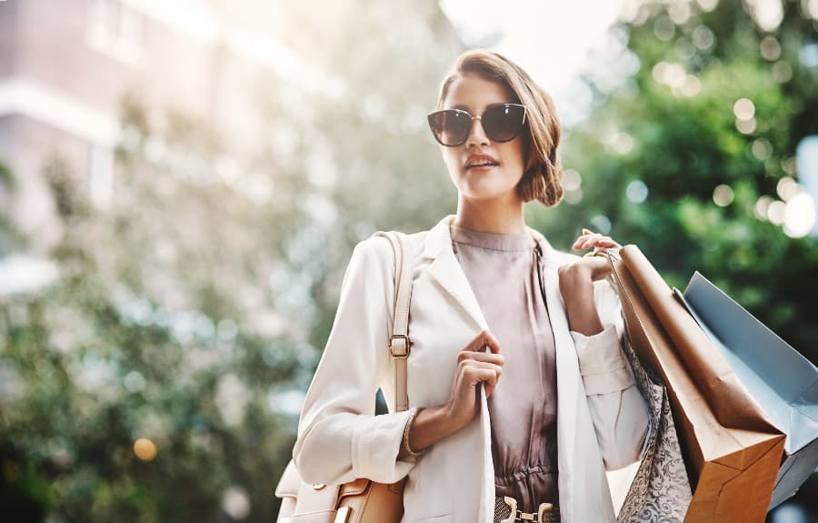 Woman wearing sunglasses and coat carrying large purse and shopping bags